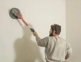 Un homme qui passe une ponceuse sur un mur blanc