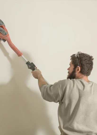 Un homme qui passe une ponceuse sur un mur blanc