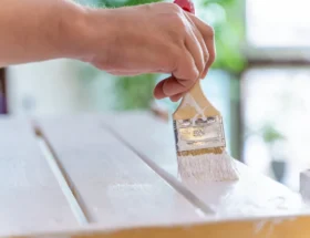 une personne qui peint un meuble en bois avec une peinture blanche
