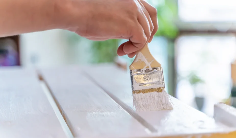 une personne qui peint un meuble en bois avec une peinture blanche