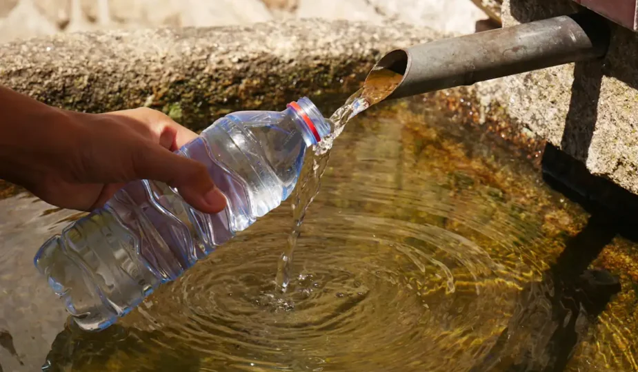 Une personne qui recueille l'eau d'un puit avec une bouteille d'eau