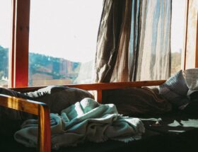 Sunlight streaming through curtains onto a cozy bed with blankets and pillows in a serene room.