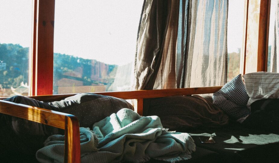 Sunlight streaming through curtains onto a cozy bed with blankets and pillows in a serene room.