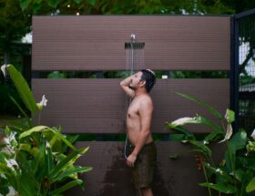 Young man enjoying an outdoor shower surrounded by lush tropical plants.
