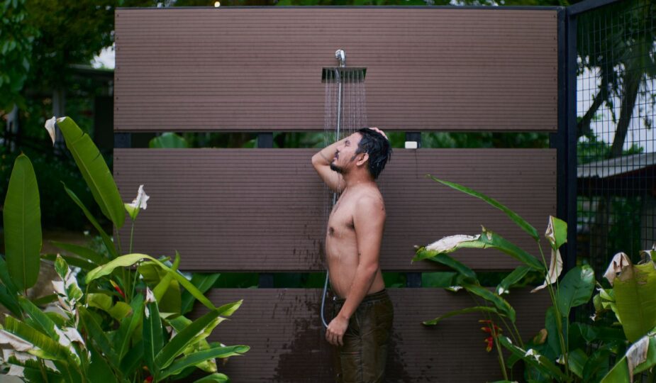 Young man enjoying an outdoor shower surrounded by lush tropical plants.