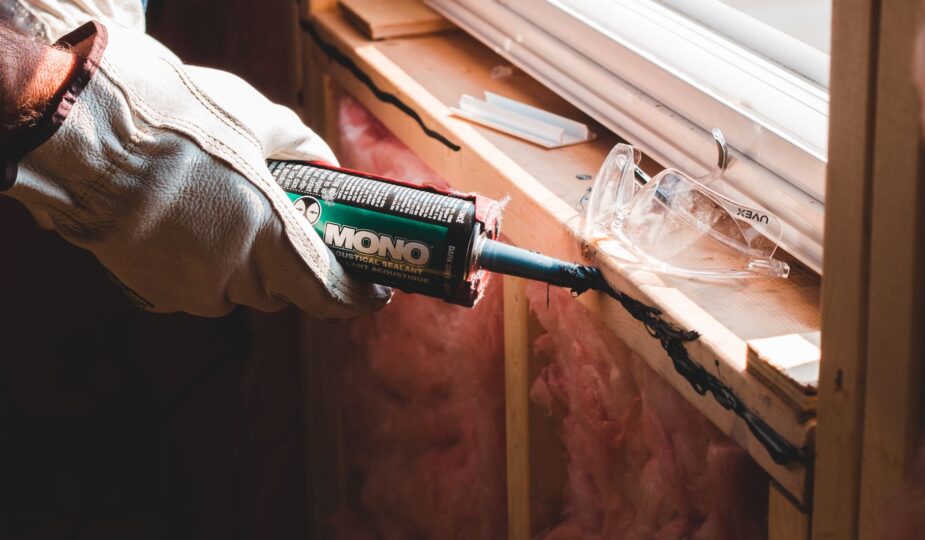 Crop unrecognizable workman in glove applying caulk from bottle on seam during window montage work in building