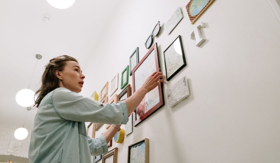 A woman arranging picture frames on a bright indoor wall.