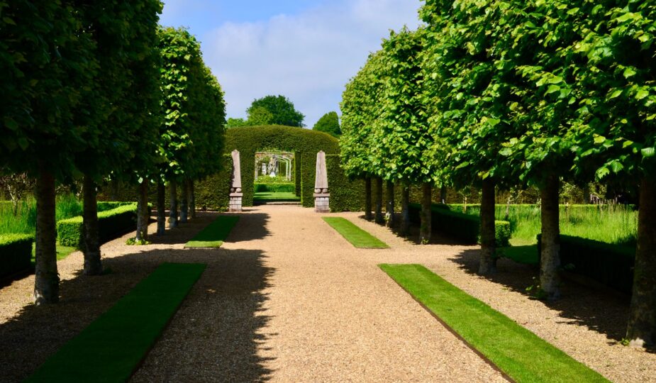 A picturesque garden pathway flanked by symmetrical trees and hedges under a clear sky.