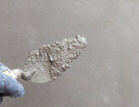 Hand wearing glove holds plaster trowel against smooth wall, depicting construction work.