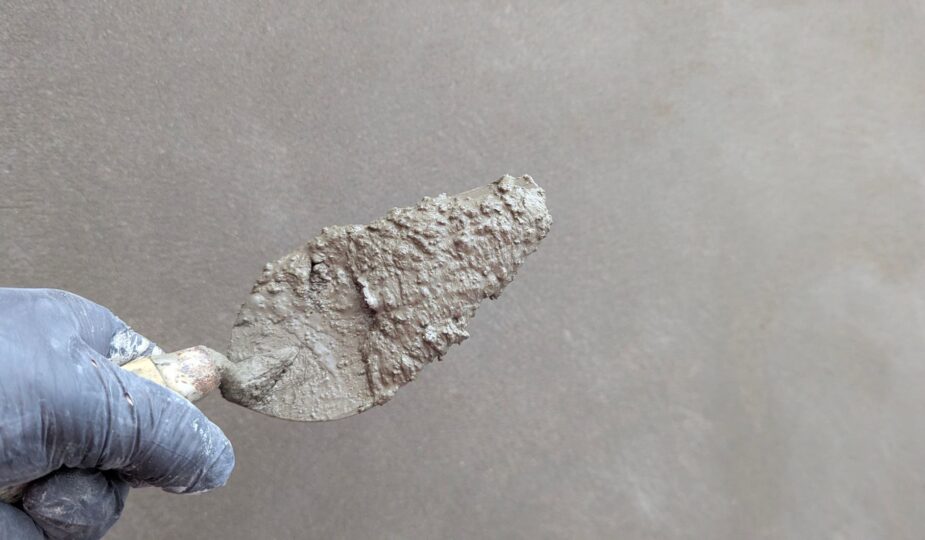 Hand wearing glove holds plaster trowel against smooth wall, depicting construction work.
