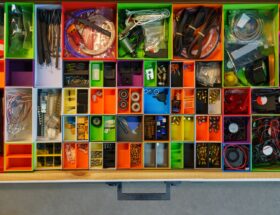 Top view of a neatly organized drawer filled with colorful containers holding various tools and electronic parts.