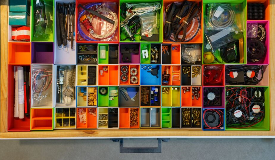 Top view of a neatly organized drawer filled with colorful containers holding various tools and electronic parts.