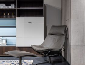 Comfortable leather chair with footrest placed on carpet near cabinet with shelves in modern flat