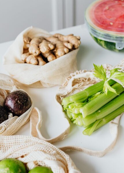 Assortment of fresh vegetables and fruits in eco-friendly net bags on a white table.