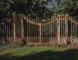 A decorative wrought iron gate framed by vibrant green trees in a serene outdoor setting.