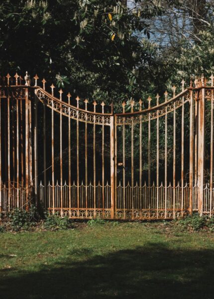 A decorative wrought iron gate framed by vibrant green trees in a serene outdoor setting.