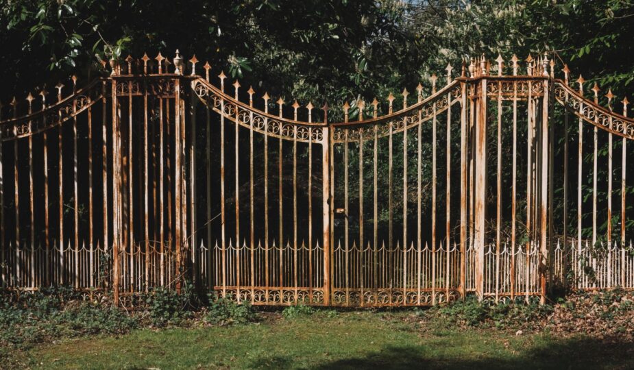 A decorative wrought iron gate framed by vibrant green trees in a serene outdoor setting.
