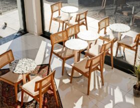 Bright cafe interior featuring wooden chairs and tables by large windows.