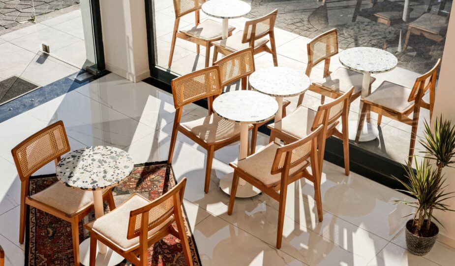 Bright cafe interior featuring wooden chairs and tables by large windows.